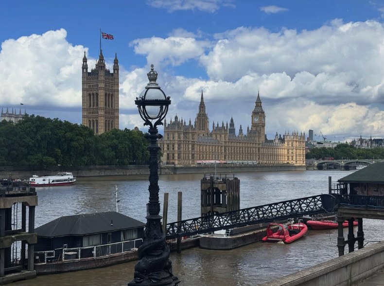The Palace of Westminster across the Thames with the Victoria Tower flying the Union flag, a pier and river craft in the foreground