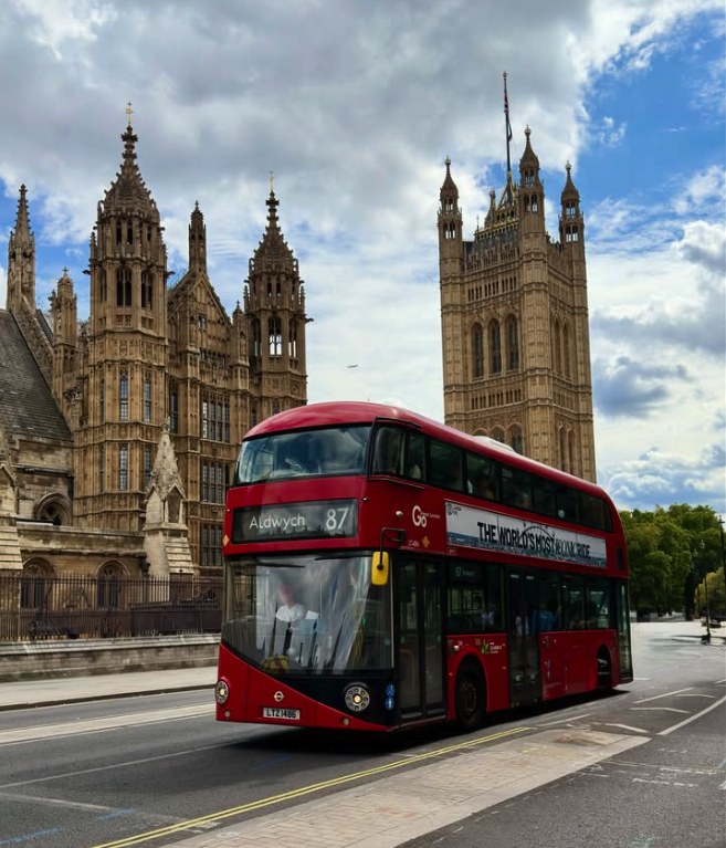 A red London bus on Abingdon Street passing the Victoria Tower at the south end of the Houses of Parliament
