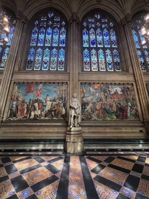 Two of the Building of Britain murals in St Stephen's Hall, with a statue between them and stained glass above