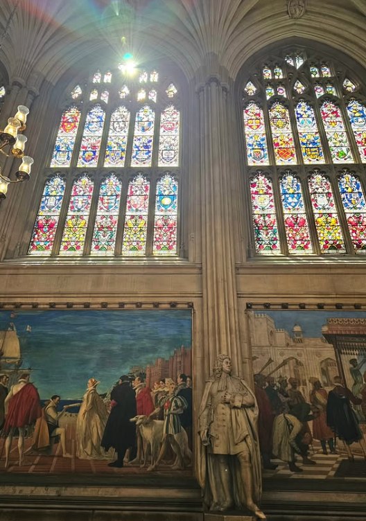 Heraldic stained glass above the murals in St Stephen's Hall, throwing colour onto the encaustic tiled floor